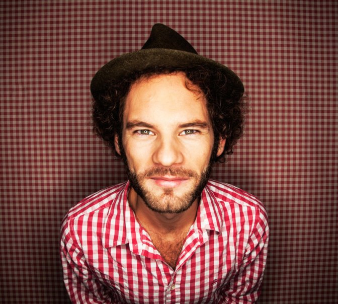 Ein Mann mit einem Hut und einem rot-wei&szlig; karierten Hemd steht vor einem passenden karierten Hintergrund und schaut direkt in die Kamera., &copy; Renitenztheater Stuttgart e.V.