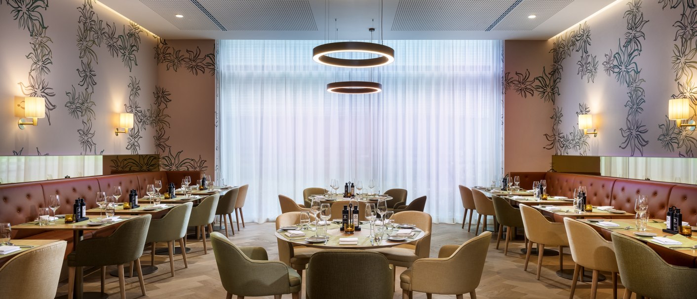 Elegantes Restaurant mit runden Tischen, modernen Leuchten und stilvoller Wanddekoration. Helle Vorhänge und gemütliche Sitzgelegenheiten schaffen eine einladende Atmosphäre., © Mövenpick Hotel Stuttgart Messe & Congress
