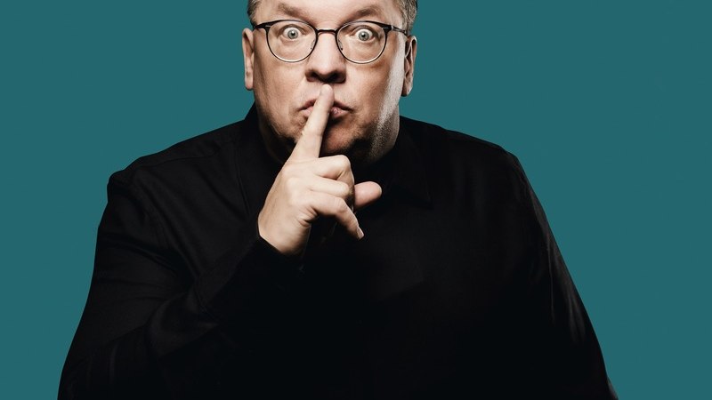 Person mit Brille und schwarzem Hemd hält den Finger vor den Mund, als Zeichen zum Schweigen, vor einem blauen Hintergrund., © Renitenztheater Stuttgart e.V. Person mit Brille und schwarzem Hemd hält den Finger vor den Mund, als Zeichen zum Schweigen, vor einem blauen Hintergrund., © Renitenztheater Stuttgart e.V.