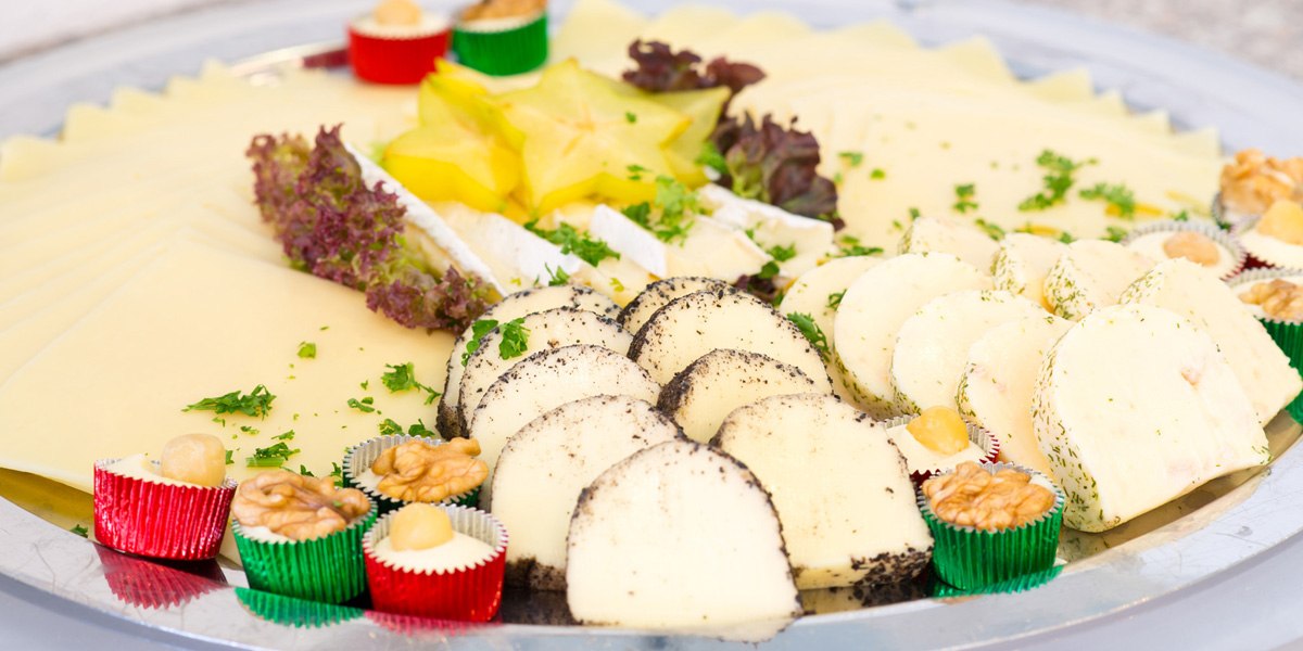 A cheese platter with a variety of cheeses, garnished with nuts, fruit, and herbs, served on a silver tray., &copy; ACHAT Hotels Deutschland