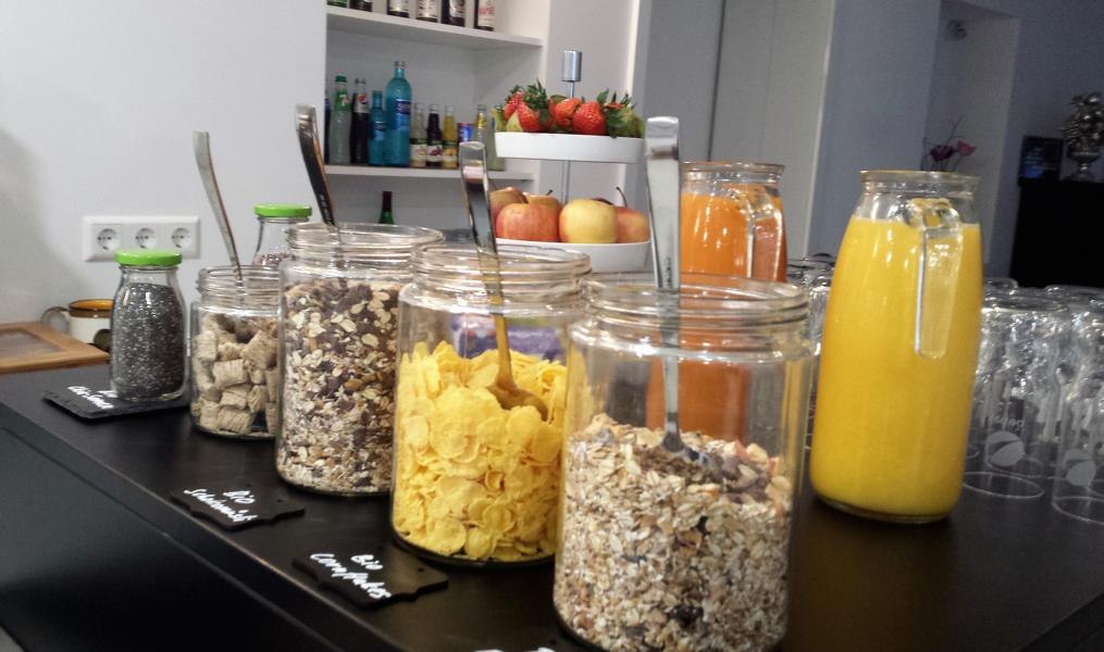 Ein Frühstücksbüffet mit Gläsern voller Müsli, Cornflakes und Säften. Im Hintergrund sind Obst und Getränke zu sehen., © TOMAS