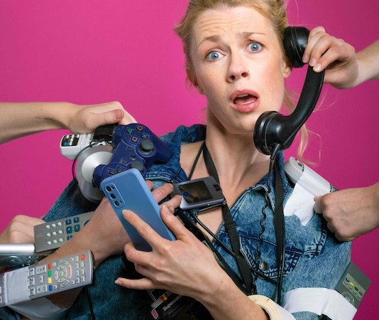 Frau in Jeansjacke hält mehrere Telefone, Fernbedienungen und ein Gamepad. Sie wirkt gestresst. Hintergrund ist pink., © Rosenau Kultur e.V. Frau in Jeansjacke hält mehrere Telefone, Fernbedienungen und ein Gamepad. Sie wirkt gestresst. Hintergrund ist pink., © Rosenau Kultur e.V.