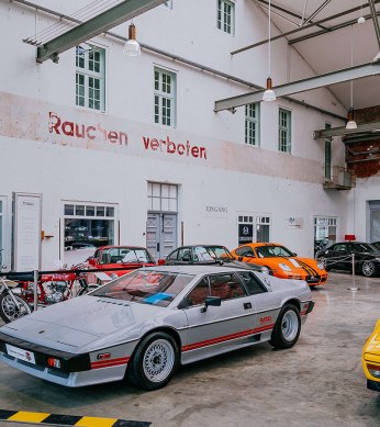 Interior view of Motorworld Region Stuttgart with classic cars and motorcycles in a hall with high ceilings and a chandelier., © Stuttgart-Marketing GmbH, Thomas Niedermüller