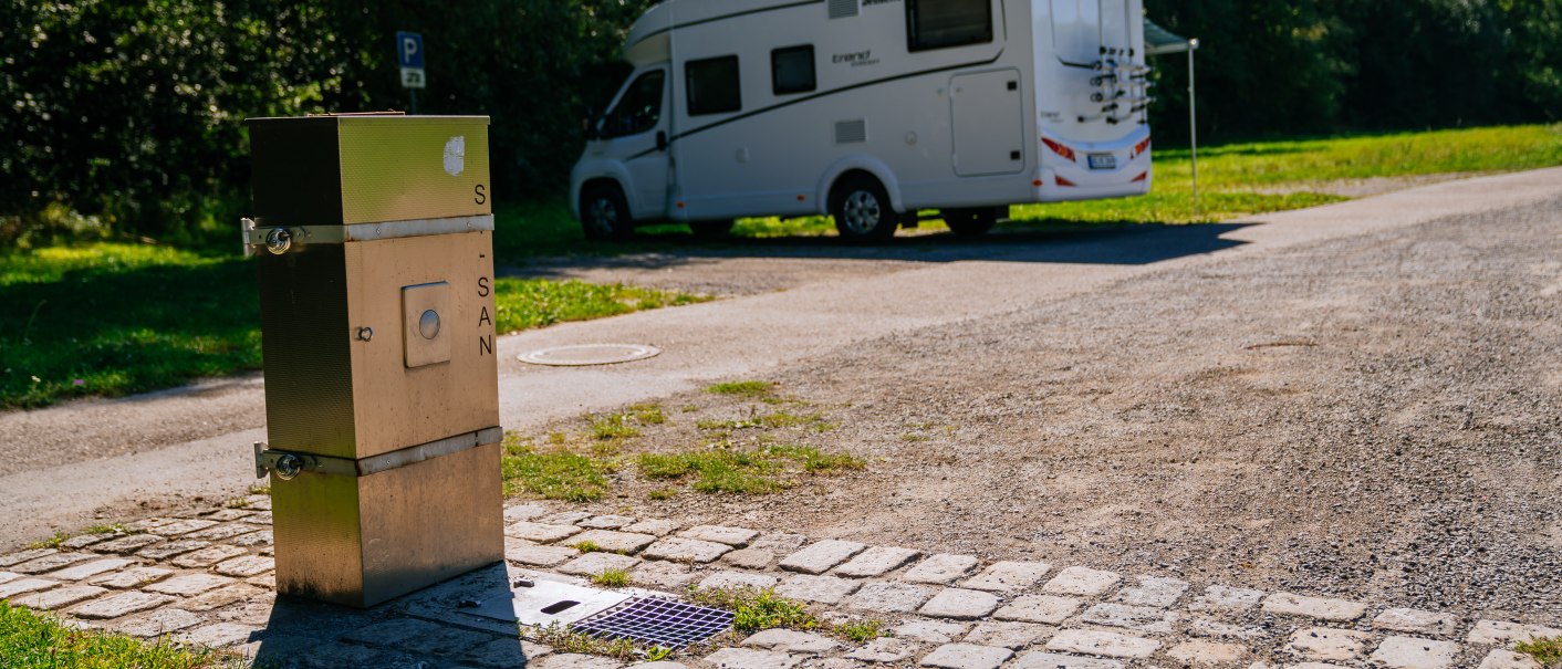 Ein Wohnmobil steht auf einem Stellplatz in Backnang. Im Vordergrund ist eine Sanitärstation zu sehen. Der Platz ist von Bäumen umgeben., © SMG, Thomas Niedermüller