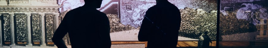 Zwei Personen stehen vor einer Multimedia-Installation, die Hegel und das Brandenburger Tor zeigt. Die Szene ist dunkel und atmosph&auml;risch beleuchtet., &copy; Julia Ochs