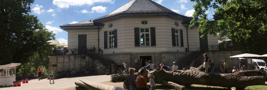 The Bärenschlössle in Stuttgart, surrounded by trees, with people relaxing and playing outside in the sunny weather., © SMG