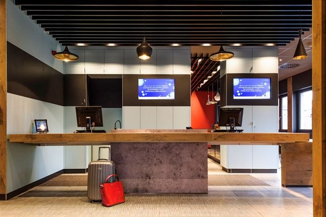 Moderne Hotelrezeption mit zwei Bildschirmen, Gepäckstücken und stilvoller Beleuchtung., © TOMAS Moderne Hotelrezeption mit zwei Bildschirmen, Gepäckstücken und stilvoller Beleuchtung., © TOMAS