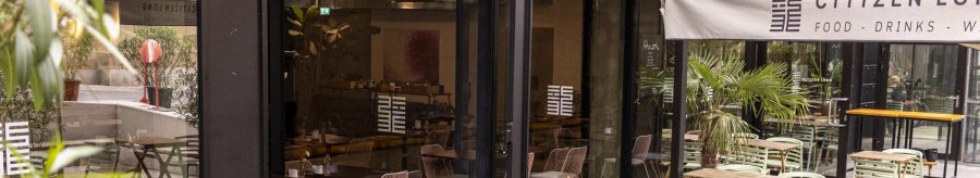 Outdoor area of a caf&eacute; with wooden tables and green chairs. An awning bears the lettering 'Citizen Long'. Plants decorate the area., &copy; SMG, Sarah Schmid