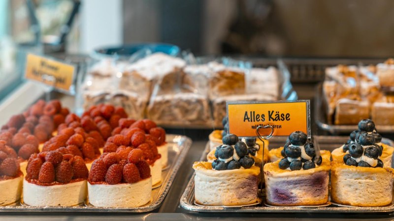Kuchen in einer Vitrine, dekoriert mit Himbeeren und Blaubeeren. Ein Schild mit der Aufschrift 'Alles K&auml;se' ist sichtbar., &copy; Stuttgart-Marketing GmbH, Sarah Schmid