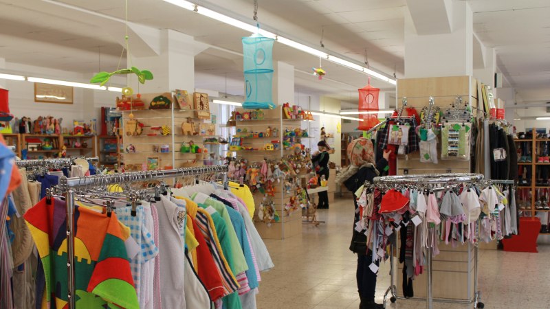 Ein Spielzeug- und Kinderbekleidungsgesch&auml;ft mit bunten Kleidungsst&uuml;cken und Spielzeugregalen. Eine Person betrachtet die ausgestellten Artikel., &copy; ZORA gGmbH