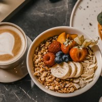 Ein Frühstückstisch mit einer Tasse Kaffee mit Herz-Latte-Art, einer Schüssel Müsli mit Früchten und einem Teller mit Waffeln und Avocado., © Fritz Stuttgart Ein Frühstückstisch mit einer Tasse Kaffee mit Herz-Latte-Art, einer Schüssel Müsli mit Früchten und einem Teller mit Waffeln und Avocado., © Fritz Stuttgart