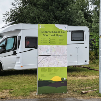 Zwei Wohnmobile parken auf einem Stellplatz im Sportpark Rems. Ein großes Schild informiert über den Standort. Im Hintergrund sind Bäume zu sehen., © Stadtverwaltung Schorndorf