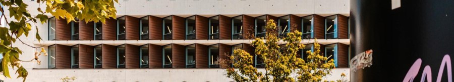 Moderne Bibliothek mit markanter geometrischer Fassade, umgeben von B&auml;umen. Ein schwarzer Pfeiler mit Graffiti ist rechts im Bild sichtbar., &copy; Stuttgart Marketing GmbH, Sarah Schmid