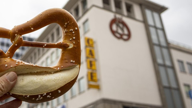 Eine Hand hält eine Brezel vor einem Gebäude mit dem Schriftzug 'Café' und einem Brezel-Logo., © Stuttgart-Marketing GmbH, Sarah Schmid Eine Hand hält eine Brezel vor einem Gebäude mit dem Schriftzug 'Café' und einem Brezel-Logo., © Stuttgart-Marketing GmbH, Sarah Schmid