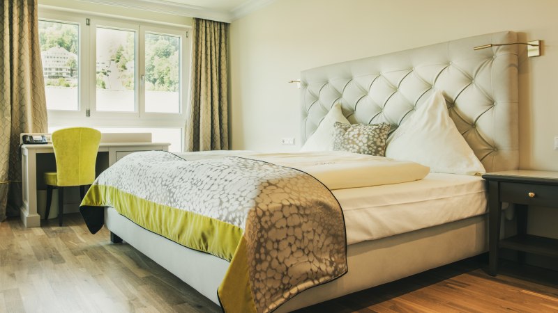Helles Hotelzimmer mit großem Bett, Schreibtisch und Blick auf Wasser und Berge durch die Fenster., © LOCHER Fotodesign & Manufaktur Helles Hotelzimmer mit großem Bett, Schreibtisch und Blick auf Wasser und Berge durch die Fenster., © LOCHER Fotodesign & Manufaktur