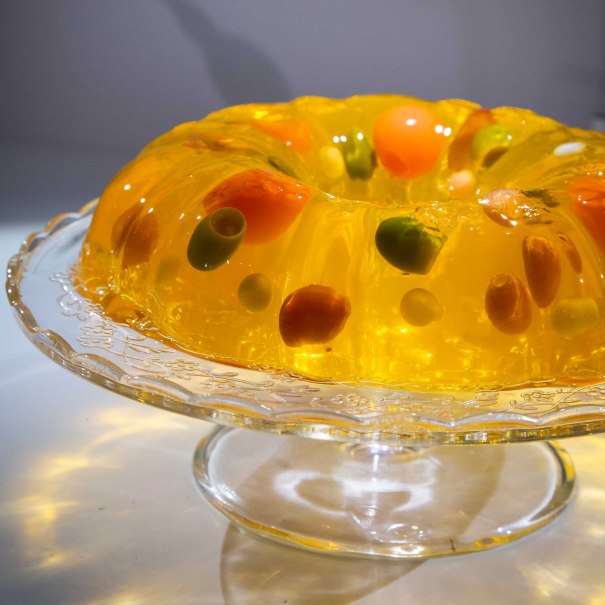 Ein Gelatine-Ring mit buntem Gemüse wie Oliven und Paprika, präsentiert auf einer dekorativen Glasplatte., © Foto: Anja Barte Telin