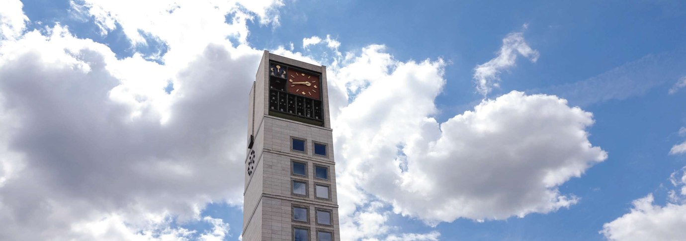 Ein modernes Gebäude mit einem hohen Uhrturm und vielen Fenstern. Der Himmel ist blau mit einigen Wolken., © Fei Shiyu Ein modernes Gebäude mit einem hohen Uhrturm und vielen Fenstern. Der Himmel ist blau mit einigen Wolken., © Fei Shiyu
