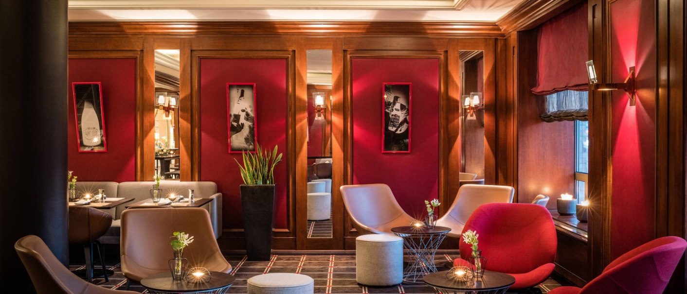 Elegant lounge at Le Méridien Stuttgart with red walls, modern armchairs and small tables. Subtle lighting and stylish decoration., © TOMAS Elegant lounge at Le Méridien Stuttgart with red walls, modern armchairs and small tables. Subtle lighting and stylish decoration., © TOMAS