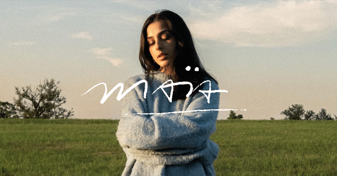 Eine Frau in einem blauen Pullover steht mit geschlossenen Augen auf einer gr&uuml;nen Wiese. Der Schriftzug 'ma&iuml;a' ist prominent im Bild., &copy; links im Bild