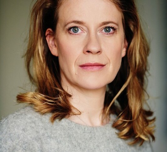 Eine Frau mit blonden Haaren und einem grauen Pullover blickt direkt in die Kamera. Der Hintergrund ist neutral gehalten., &copy; Theaterhaus Stuttgart e.V.