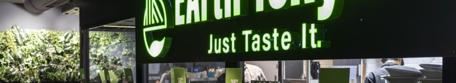 Restaurant mit grünem Leuchtschild 'EArth Tokyo' und dem Slogan 'Just Taste It'. Moderne Einrichtung mit Pflanzenwand., © SMG, Sarah Schmid