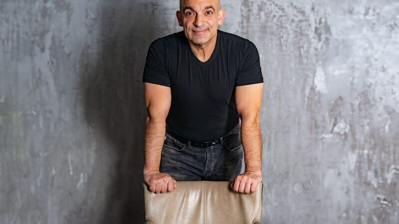 Mann in schwarzem T-Shirt lehnt auf Stuhl mit Aufschrift 'Am Ende vorn!' vor grauer Wand., © Theaterhaus Stuttgart e.V. Mann in schwarzem T-Shirt lehnt auf Stuhl mit Aufschrift 'Am Ende vorn!' vor grauer Wand., © Theaterhaus Stuttgart e.V.