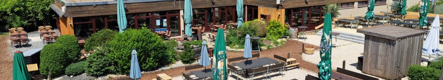 Outdoor area of Weitmann's Waldhaus with wooden tables, benches and parasols, surrounded by green trees and blue sky., &copy; Timo Weitmann
