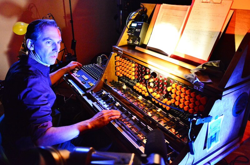 A musician plays a unique instrument with numerous buttons and keys, surrounded by sheet music and technical equipment., &copy; Theaterhaus Stuttgart e.V.