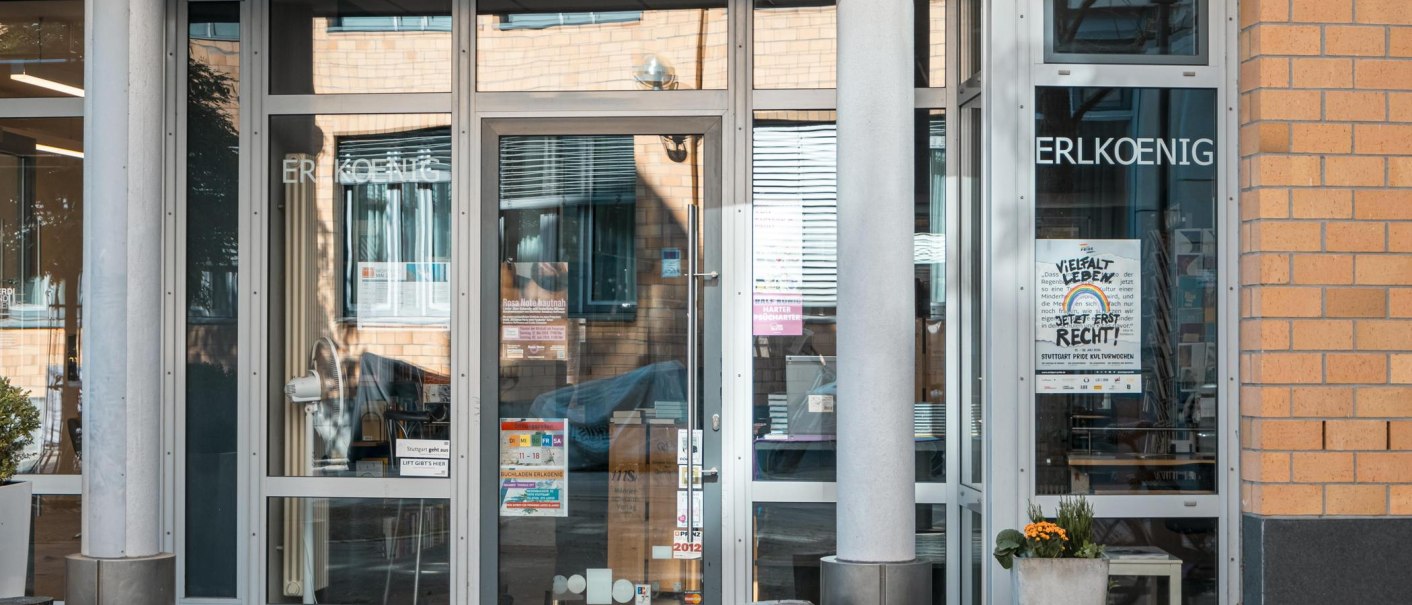 Eingang eines Geb&auml;udes mit Glast&uuml;ren, auf denen 'ERLKOENIG' steht. Poster und Pflanzen sind sichtbar. Moderne Architektur mit Backsteinfassade., &copy; SMG, Sarah Schmid