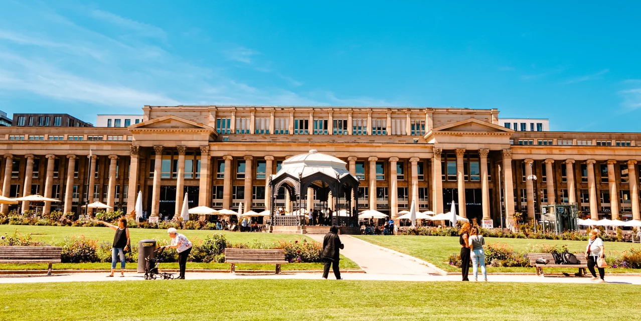 Königsbau in Stuttgart mit klassischer Fassade, Grünanlage und Spaziergängern bei sonnigem Wetter., © SMG, Sarah Schmid Königsbau in Stuttgart mit klassischer Fassade, Grünanlage und Spaziergängern bei sonnigem Wetter., © SMG, Sarah Schmid