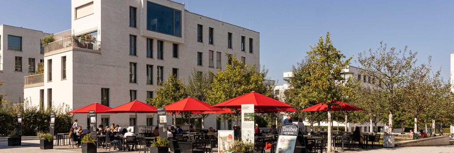 Moderne Wohngebäude in Stuttgart Killesberghöhe, mit roten Sonnenschirmen und Menschen auf einem Platz bei sonnigem Wetter., © Stuttgart-Marketing GmbH, Sarah Schmid Moderne Wohngebäude in Stuttgart Killesberghöhe, mit roten Sonnenschirmen und Menschen auf einem Platz bei sonnigem Wetter., © Stuttgart-Marketing GmbH, Sarah Schmid