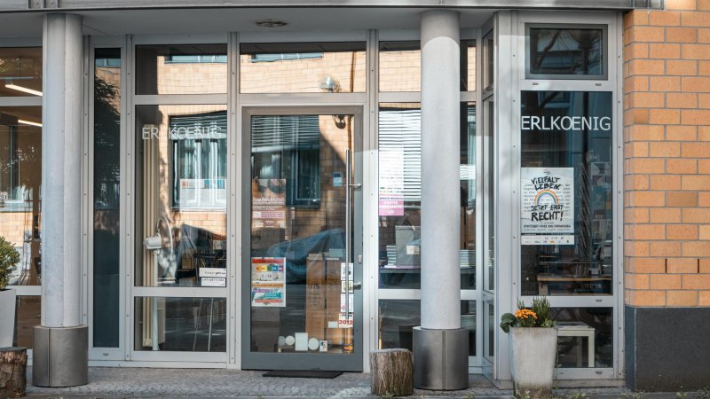 Eingang eines Gebäudes mit Glastüren, auf denen 'ERLKOENIG' steht. Poster und Pflanzen sind sichtbar. Moderne Architektur mit Backsteinfassade., © SMG, Sarah Schmid Eingang eines Gebäudes mit Glastüren, auf denen 'ERLKOENIG' steht. Poster und Pflanzen sind sichtbar. Moderne Architektur mit Backsteinfassade., © SMG, Sarah Schmid