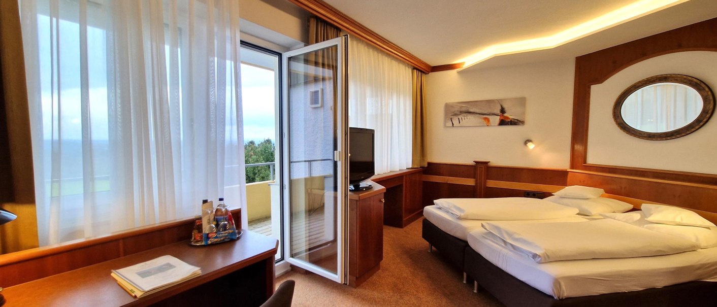 A cozy hotel room with a double bed, a desk, and a balcony. Large windows let in plenty of light, and there is a mirror hanging on the wall., © TOMAS A cozy hotel room with a double bed, a desk, and a balcony. Large windows let in plenty of light, and there is a mirror hanging on the wall., © TOMAS