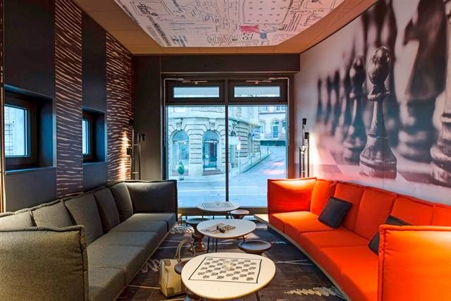 Modern room with gray and red sofas, chessboard pattern on table, wall with chess pieces, window with view of building., &copy; TOMAS
