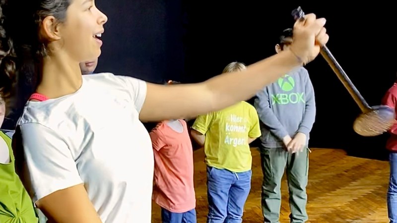 Kinder stehen auf einer B&uuml;hne bei einer Generalprobe. Ein M&auml;dchen h&auml;lt ein Mikrofon und scheint zu singen oder zu sprechen., &copy; Tathea - Lena Oschowitzer