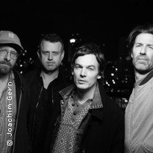 Vier Männer posieren vor einer nächtlichen Stadtkulisse. Schwarz-weiß Foto, entspannte Atmosphäre., © links im Bild