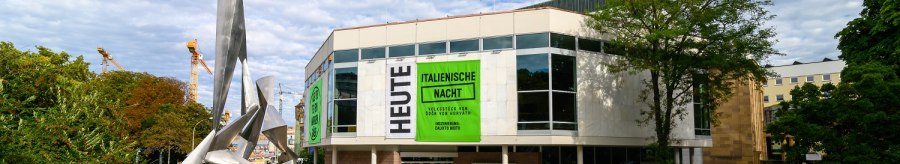 Moderne Skulptur vor dem Schauspielhaus mit gro&szlig;en Fenstern und Plakaten f&uuml;r 'Italienische Nacht'. Wolkenbedeckter Himmel, B&auml;ume und Baukr&auml;ne im Hintergrund., &copy; Bj&ouml;rn Klein