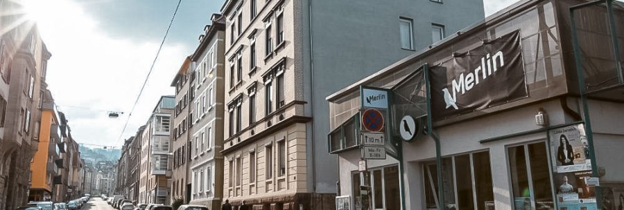 Stra&szlig;enszene in Stuttgart mit dem Kulturzentrum Merlin e.V. rechts im Bild. Die Sonne scheint, Autos parken entlang der Stra&szlig;e., &copy; Merlin, Stuttgart