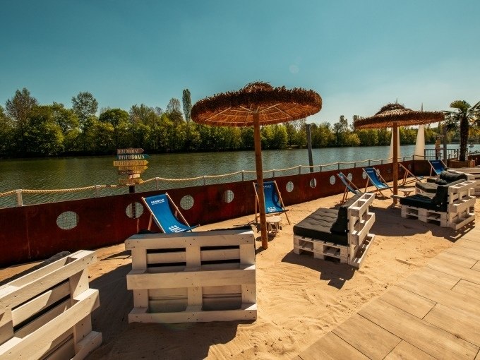 Beach area with pallet furniture, parasols and sun loungers on the riverbank, surrounded by trees and clear skies., &copy; Cool-Tours StattReisen