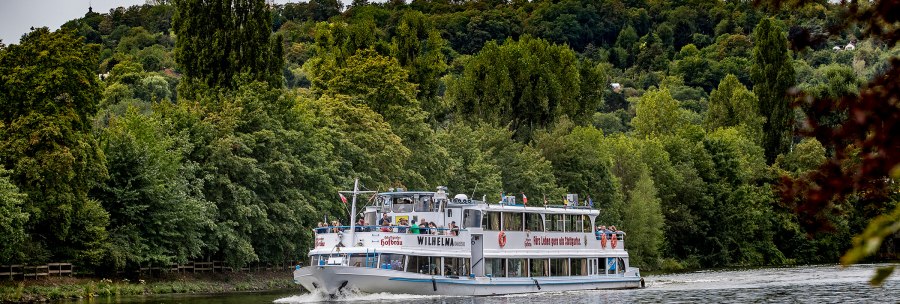 The Wilhelma excursion boat sails along a river surrounded by dense forest and green hills., © all copyrights are reserved by maks richter