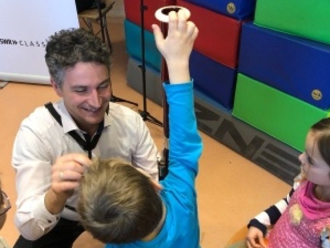 Ein Mann l&auml;chelt und interagiert mit zwei Kindern in einem Raum mit bunten Matten im Hintergrund., &copy; Landesmuseum W&uuml;rttemberg