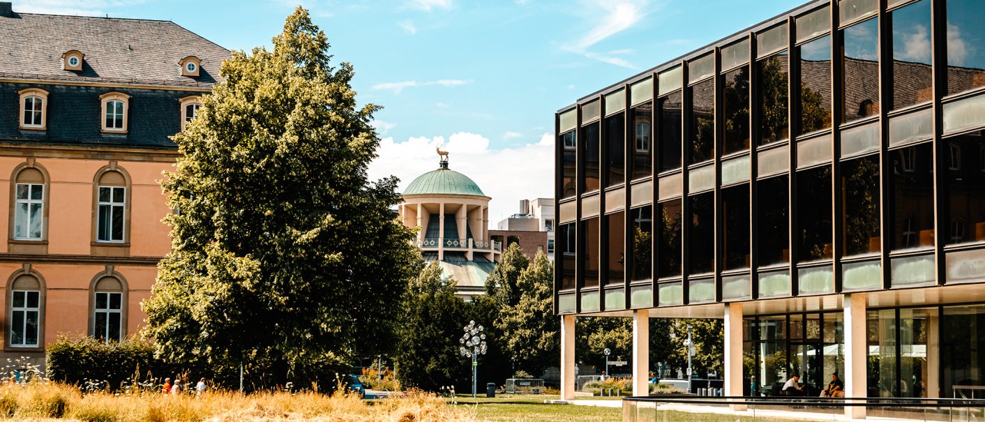 Ein modernes Gebäude mit Glasfassade neben einem historischen Gebäude, umgeben von Bäumen und einem blauen Himmel., © Stuttgart-Marketing GmbH, Sarah Schmid