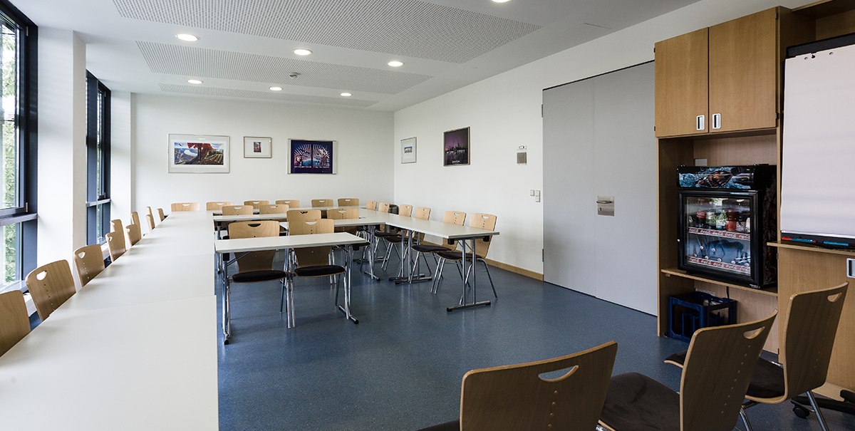 Seminar room with U-shaped tables and chairs, pictures on the wall, fridge in the corner, bright lighting., © TOMAS Seminar room with U-shaped tables and chairs, pictures on the wall, fridge in the corner, bright lighting., © TOMAS