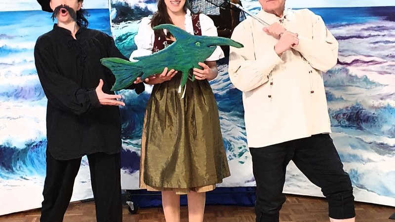 Drei Personen in Kostümen posieren vor einem maritimen Hintergrund. Eine Person hält einen grünen Pappfisch, die anderen tragen Fischerbekleidung., © Michael Kunze, Theater Tredeschin Drei Personen in Kostümen posieren vor einem maritimen Hintergrund. Eine Person hält einen grünen Pappfisch, die anderen tragen Fischerbekleidung., © Michael Kunze, Theater Tredeschin