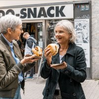 Zwei Frauen genießen Burger vor dem Imbiss 'UDO SNACK' in einer belebten Straße. Sie lachen und unterhalten sich., © Stuttgart Marketing GmbH - Sarah Schmid Zwei Frauen genießen Burger vor dem Imbiss 'UDO SNACK' in einer belebten Straße. Sie lachen und unterhalten sich., © Stuttgart Marketing GmbH - Sarah Schmid