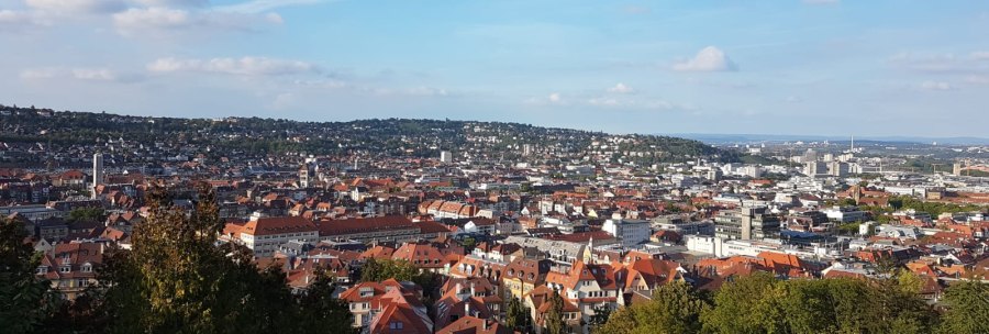Panoramablick auf eine Stadt mit roten Dächern, umgeben von grünen Hügeln und blauem Himmel., © SMG