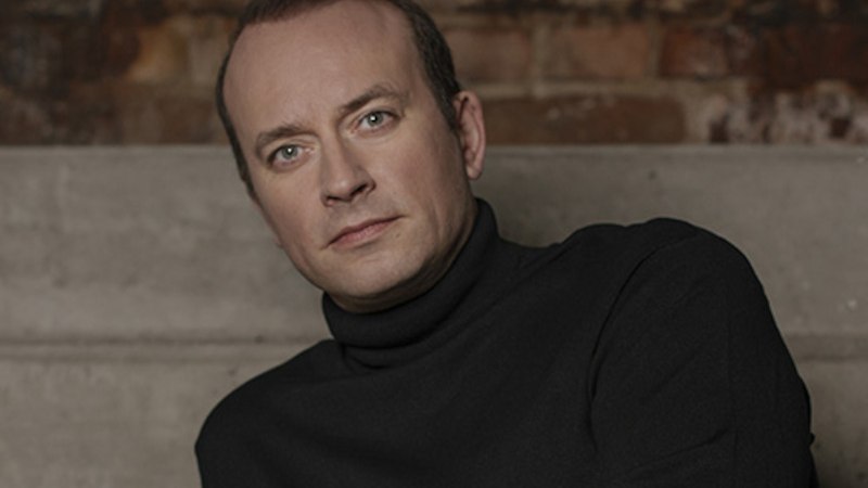 Ein Mann in schwarzem Rollkragenpullover sitzt vor einer Backsteinwand. Er hat einen ernsten Gesichtsausdruck und schaut direkt in die Kamera., © Internationale Hugo-Wolf-Akademie Ein Mann in schwarzem Rollkragenpullover sitzt vor einer Backsteinwand. Er hat einen ernsten Gesichtsausdruck und schaut direkt in die Kamera., © Internationale Hugo-Wolf-Akademie