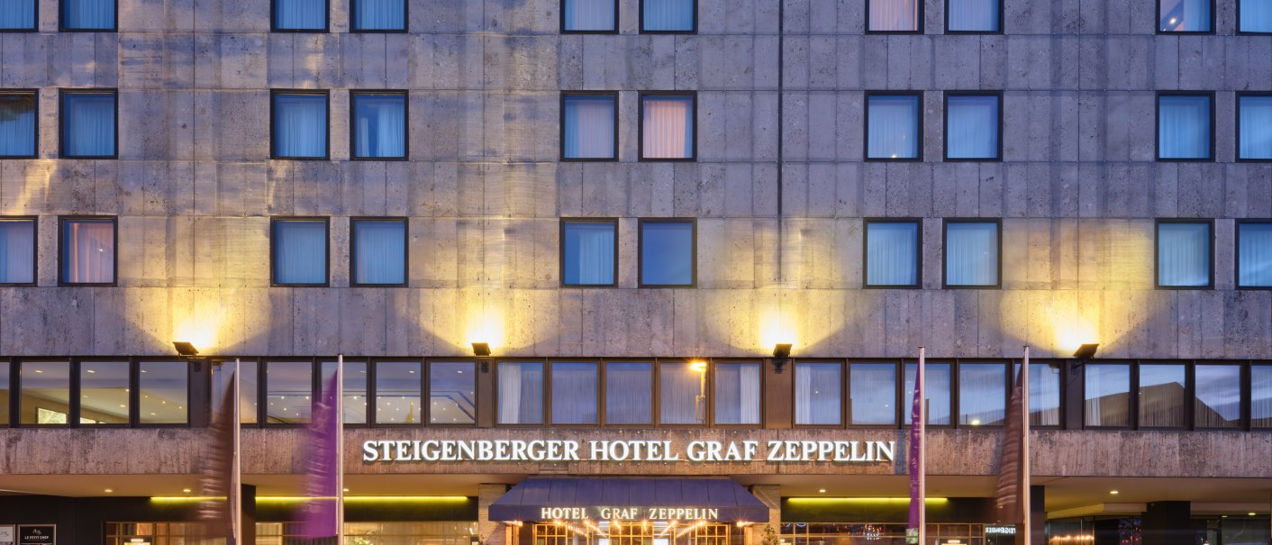 The Steigenberger Hotel Graf Zeppelin at dusk. The façade is illuminated and traces of light from cars are visible on the street., © Steigenberger Graf Zeppelin The Steigenberger Hotel Graf Zeppelin at dusk. The façade is illuminated and traces of light from cars are visible on the street., © Steigenberger Graf Zeppelin