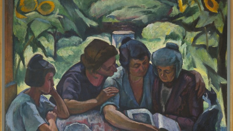 Vier Frauen sitzen an einem Tisch und lesen gemeinsam ein Buch. Im Hintergrund sind grüne Pflanzen und Sonnenblumen zu sehen. Ein schwarzer Hund sitzt daneben., © Jozsef Böhm Vier Frauen sitzen an einem Tisch und lesen gemeinsam ein Buch. Im Hintergrund sind grüne Pflanzen und Sonnenblumen zu sehen. Ein schwarzer Hund sitzt daneben., © Jozsef Böhm