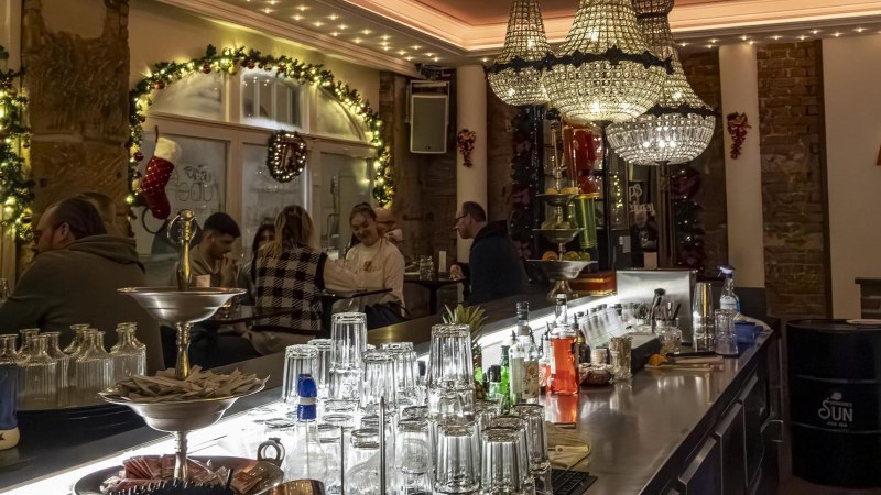 Festlich dekorierte Bar mit Kronleuchtern, Gläsern und Getränken auf der Theke. Gäste sitzen und unterhalten sich in gemütlicher Atmosphäre., © Stuttgart Marketing GmbH, Sarah Schmid
